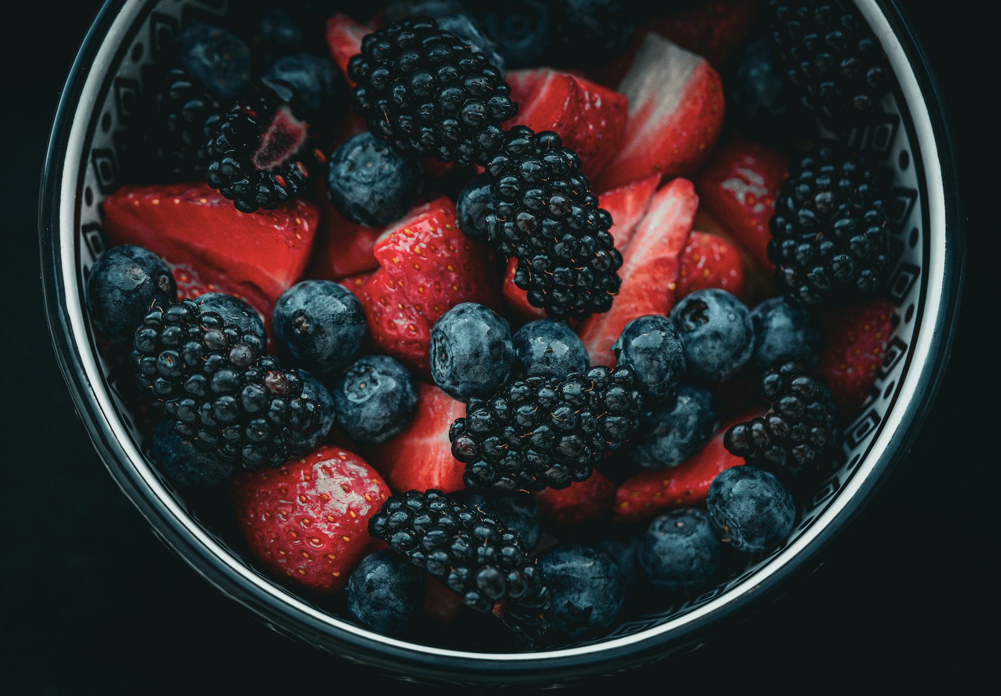 A bowl of blackberries, blueberries and strawberries on a dark background