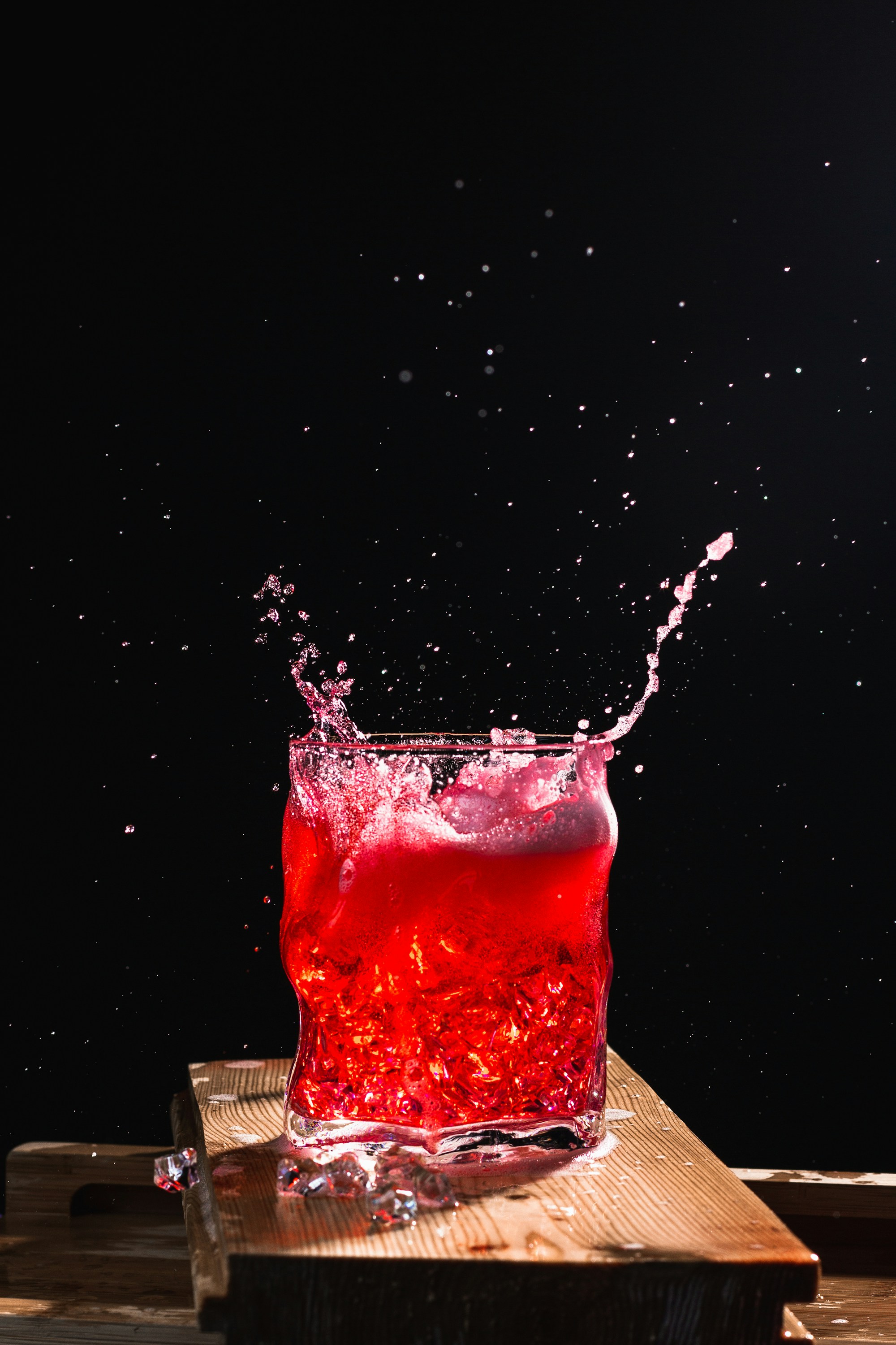 Bright red juice splashing out of a glass against black